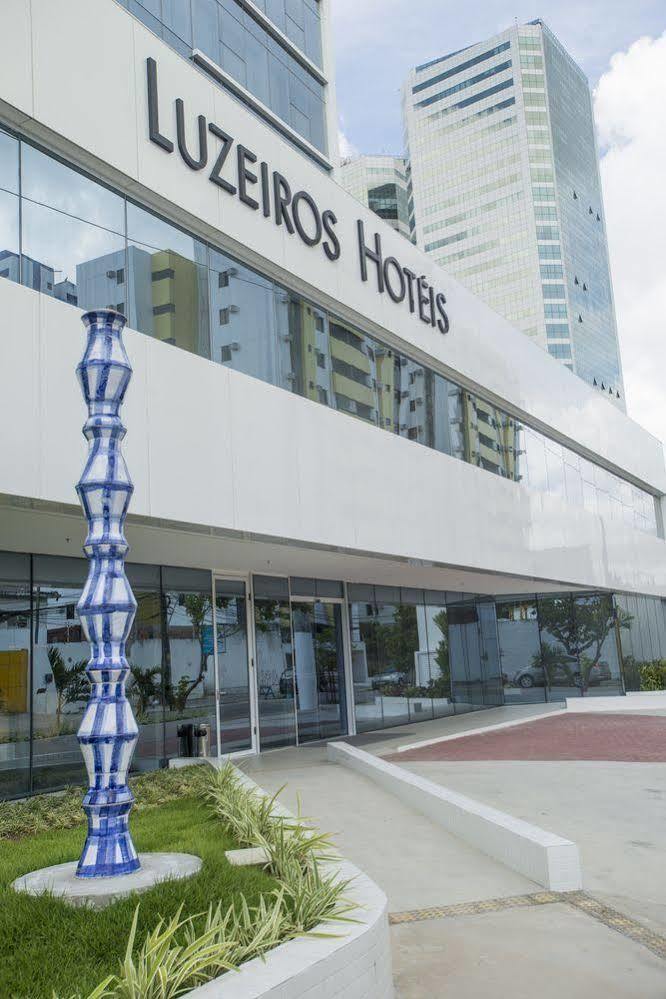 Hotel Luzeiros Recife Zewnętrze zdjęcie The photo shows a modern hotel building with large glass windows and a sleek, white facade. In front of the hotel, there is a tall, decorative sculpture that features a unique, twisting shape with a blue and white color scheme. The hotel name is prom